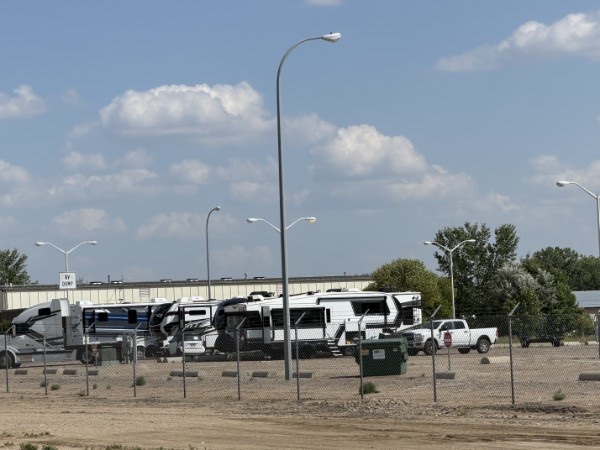 Fifth-wheel trailers packed behind a chain-link fence at the Steerage Life section of the 2026 Airstream International Rally in Minot, North Dakota, with a dumpster and an RV dump sign.